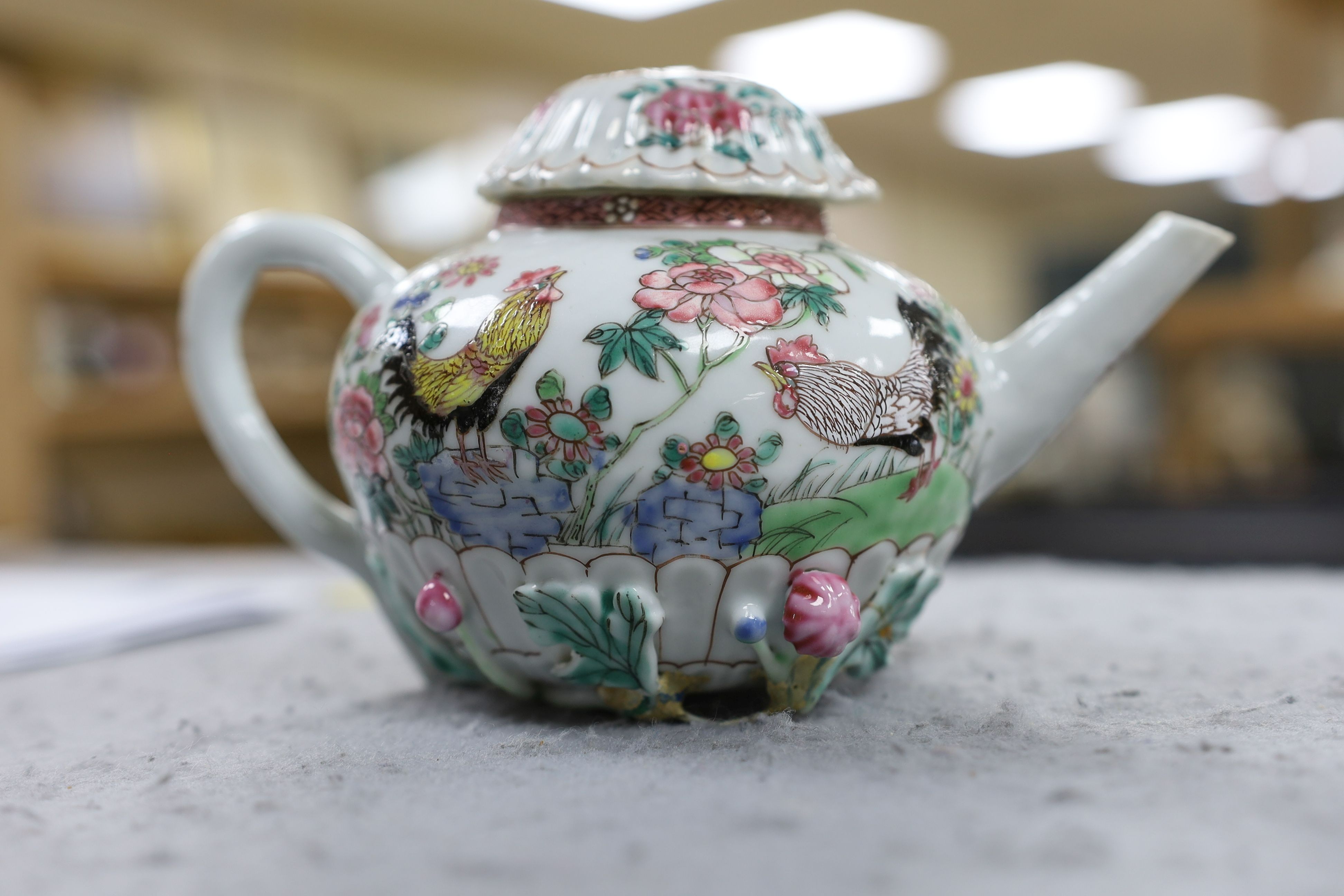 A Chinese famille rose chrysanthemum moulded teapot, early Qianlong period, painted with a cockerel amongst flowers, on a cage work base, 10 cms high
